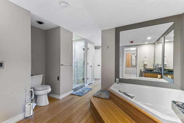 full bathroom featuring a shower stall, toilet, a garden tub, wood finished floors, and vanity