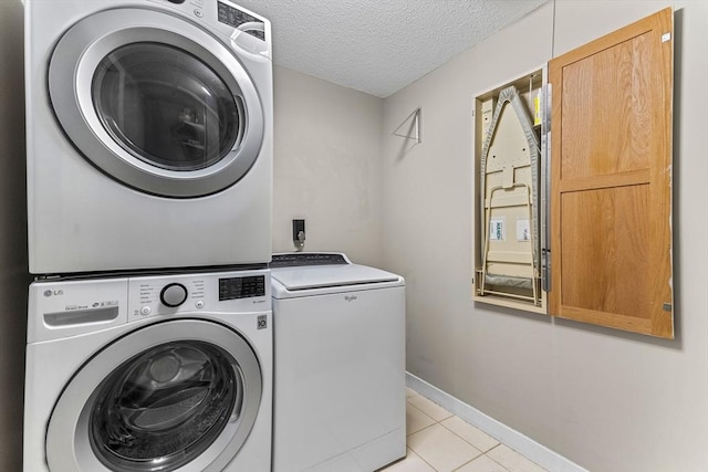 washroom featuring light tile patterned floors, baseboards, stacked washing maching and dryer, cabinet space, and a textured ceiling