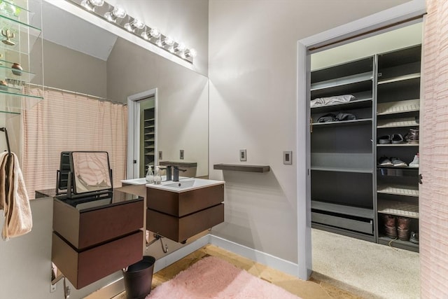 full bath with curtained shower, vanity, a walk in closet, and baseboards