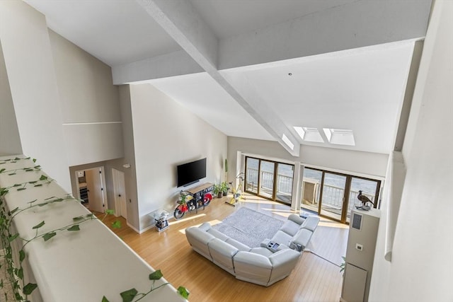 living area featuring beam ceiling, a skylight, wood finished floors, and high vaulted ceiling