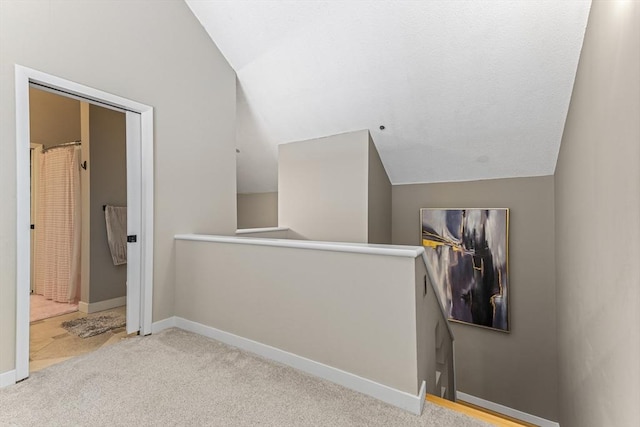 hallway with an upstairs landing, carpet floors, baseboards, and vaulted ceiling