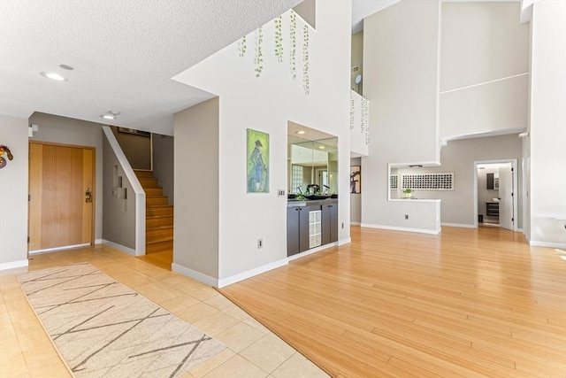 unfurnished living room with stairs, wood finished floors, baseboards, and a textured ceiling