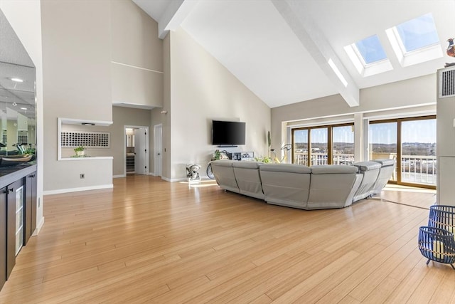 living room with a skylight, light wood-style flooring, baseboards, and high vaulted ceiling