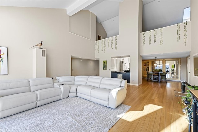 living area featuring beamed ceiling, baseboards, high vaulted ceiling, and wood finished floors