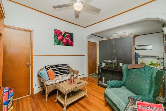 sitting room with ceiling fan, baseboard heating, arched walkways, wood finished floors, and ornamental molding