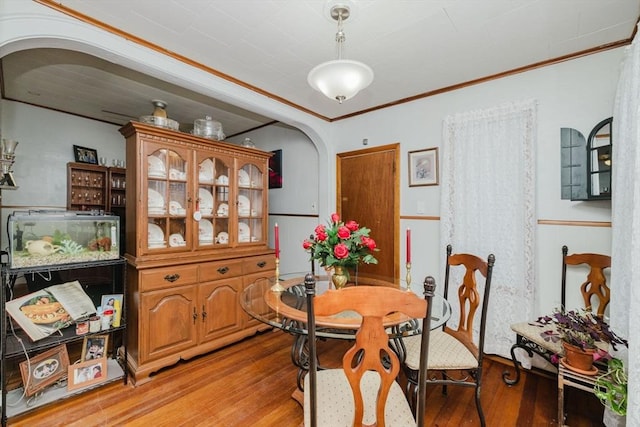 dining space featuring arched walkways, light wood-style flooring, wainscoting, and ornamental molding