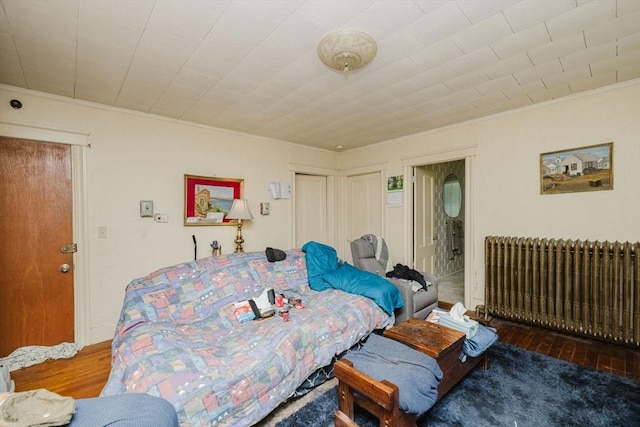 bedroom featuring wood-type flooring, crown molding, a closet, radiator heating unit, and connected bathroom