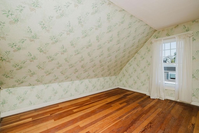 additional living space featuring baseboards, lofted ceiling, hardwood / wood-style flooring, and wallpapered walls