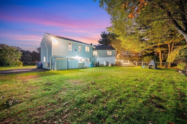 back house at dusk with central air condition unit and a lawn