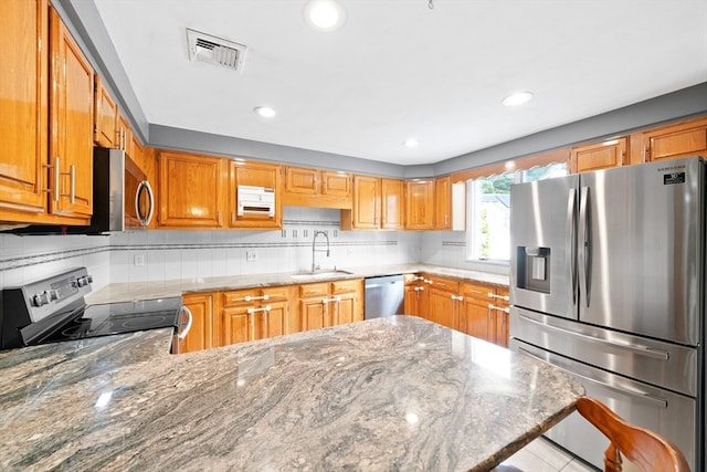 kitchen with light stone countertops, appliances with stainless steel finishes, sink, and decorative backsplash