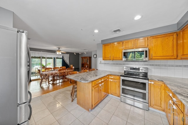 kitchen featuring kitchen peninsula, ceiling fan, a breakfast bar, light tile patterned flooring, and stainless steel appliances