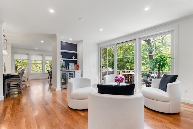 living room featuring light wood-type flooring, built in shelves, beverage cooler, recessed lighting, and crown molding