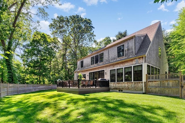 rear view of property with a lawn, a shingled roof, a deck, and fence