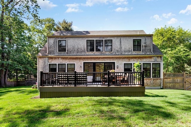 rear view of property featuring a lawn, roof with shingles, a deck, and fence