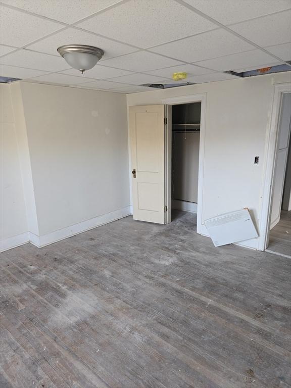 unfurnished bedroom with a closet, a drop ceiling, wood finished floors, and baseboards