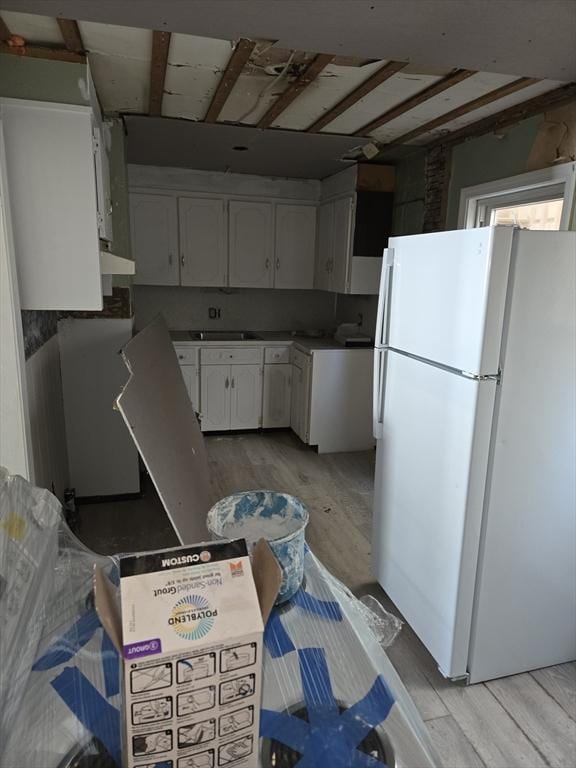 kitchen with under cabinet range hood, light wood-style flooring, freestanding refrigerator, and white cabinetry