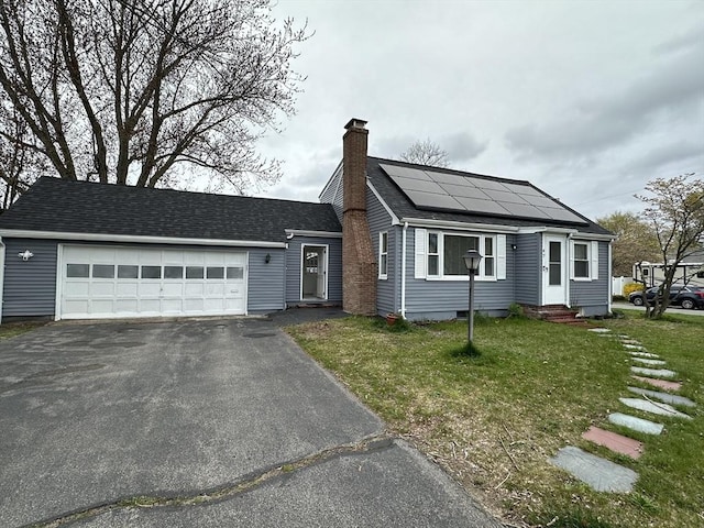 view of front of home featuring an attached garage, a chimney, a front lawn, aphalt driveway, and roof mounted solar panels