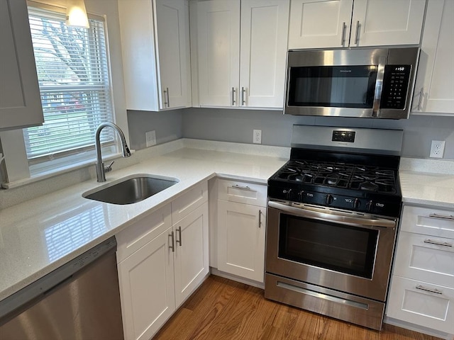 kitchen with wood finished floors, white cabinets, stainless steel appliances, and a sink