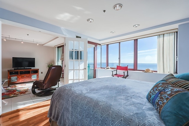 bedroom with a water view, rail lighting, and wood-type flooring