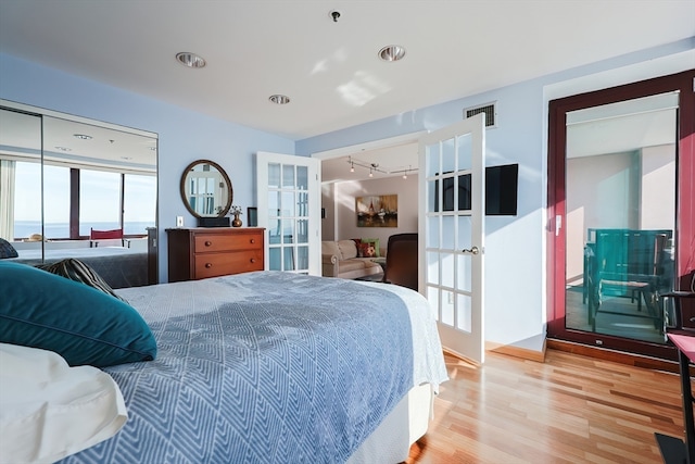 bedroom featuring french doors, hardwood / wood-style flooring, a water view, and rail lighting