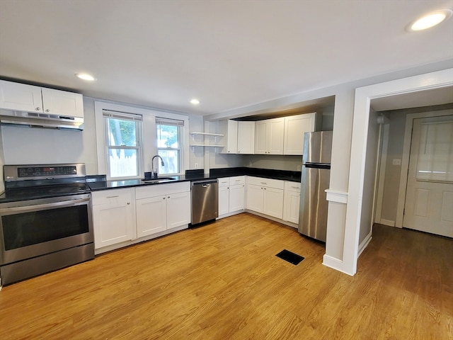 kitchen with appliances with stainless steel finishes, white cabinetry, sink, and light hardwood / wood-style floors