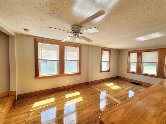 unfurnished room with light wood-type flooring, a textured ceiling, plenty of natural light, and ceiling fan