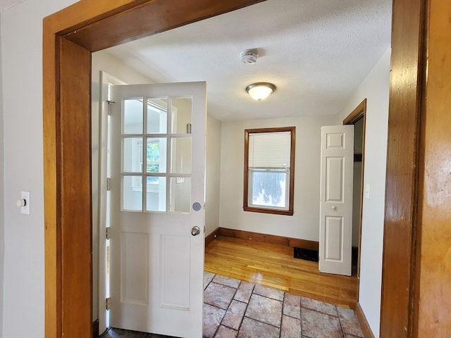 doorway to outside with light wood-type flooring and a textured ceiling