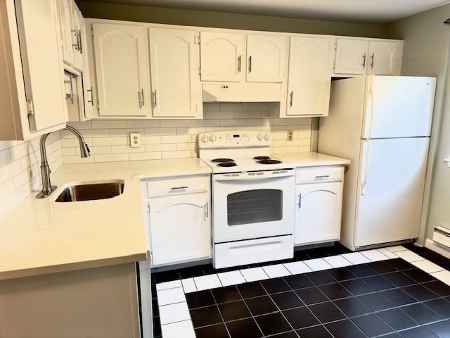 kitchen featuring decorative backsplash, white appliances, dark tile patterned floors, sink, and white cabinetry