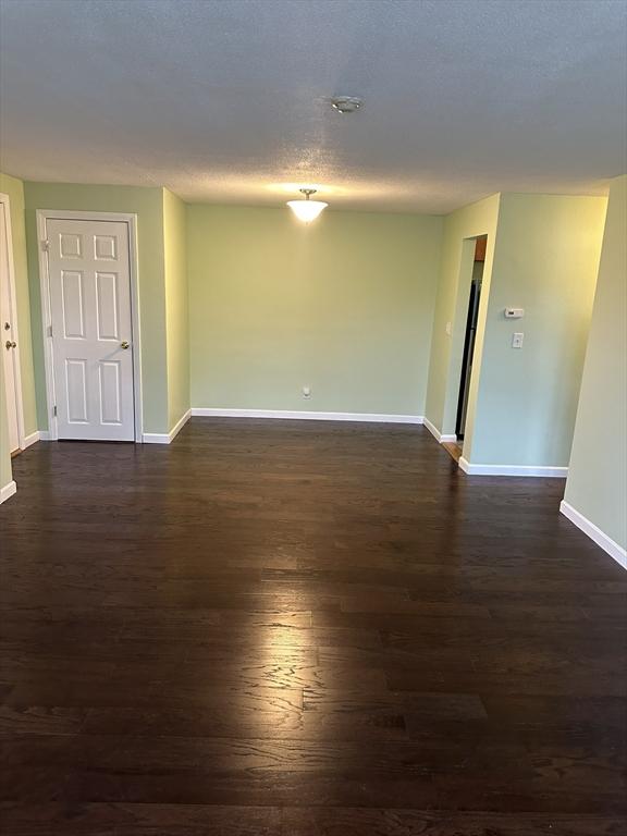 unfurnished room with dark wood-style flooring, a textured ceiling, and baseboards