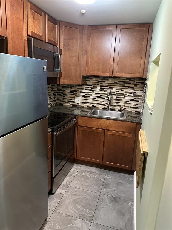 kitchen with appliances with stainless steel finishes, dark countertops, a sink, and decorative backsplash