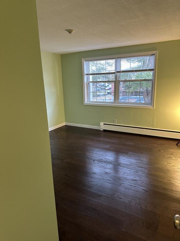 empty room with a healthy amount of sunlight, baseboard heating, and dark wood-type flooring