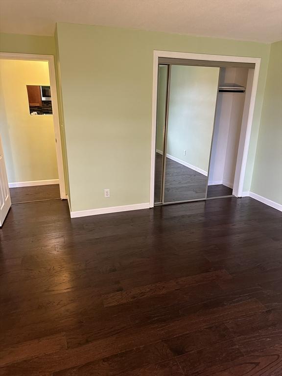 unfurnished bedroom featuring dark wood-style floors, a closet, and baseboards