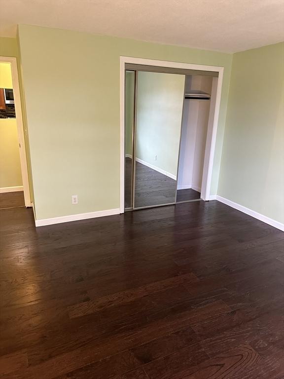 unfurnished bedroom featuring a closet, dark wood finished floors, and baseboards