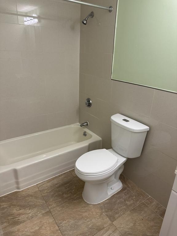 full bathroom featuring tub / shower combination, toilet, and tile walls