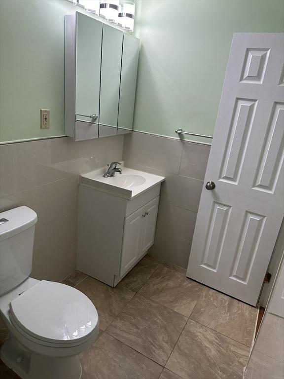 bathroom featuring a wainscoted wall, toilet, tile walls, and vanity