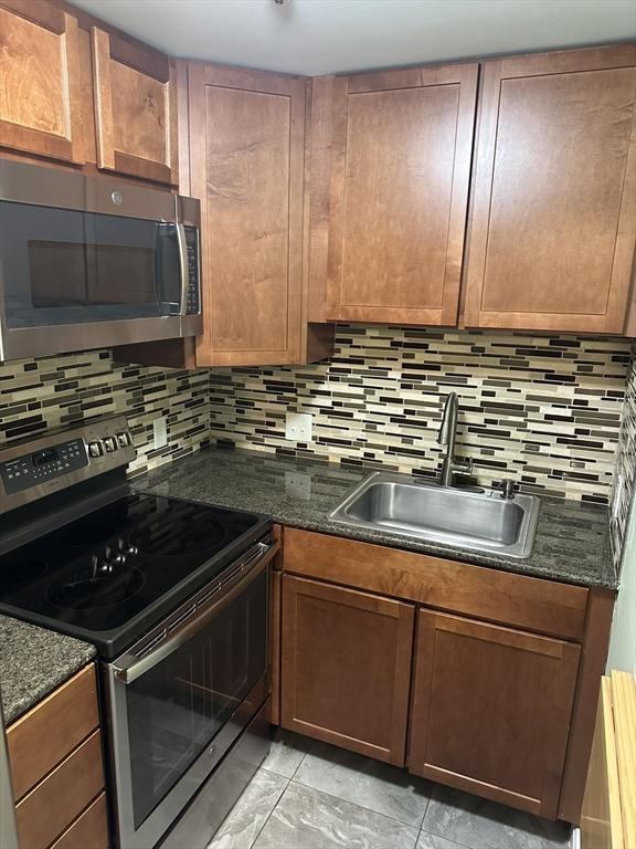 kitchen with appliances with stainless steel finishes, dark stone counters, a sink, and backsplash