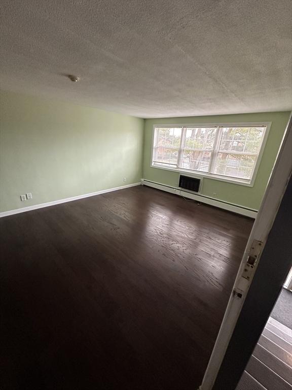 empty room with a textured ceiling, baseboards, and dark wood-type flooring