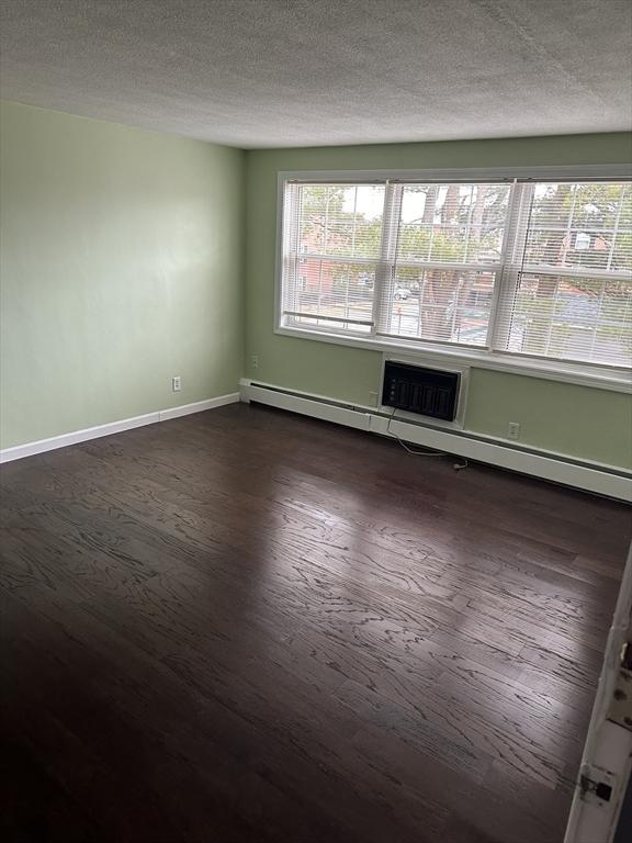 unfurnished room featuring a textured ceiling, dark wood-type flooring, a baseboard radiator, and baseboards