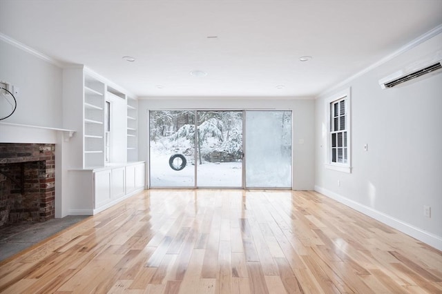 unfurnished living room with built in shelves, light hardwood / wood-style floors, a brick fireplace, crown molding, and a wall mounted air conditioner