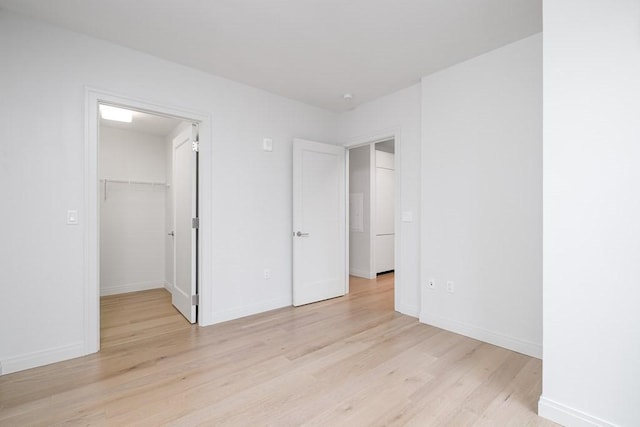 unfurnished bedroom with a walk in closet, light wood-style floors, baseboards, and a closet