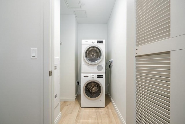 clothes washing area featuring laundry area, baseboards, stacked washer and clothes dryer, and light wood finished floors