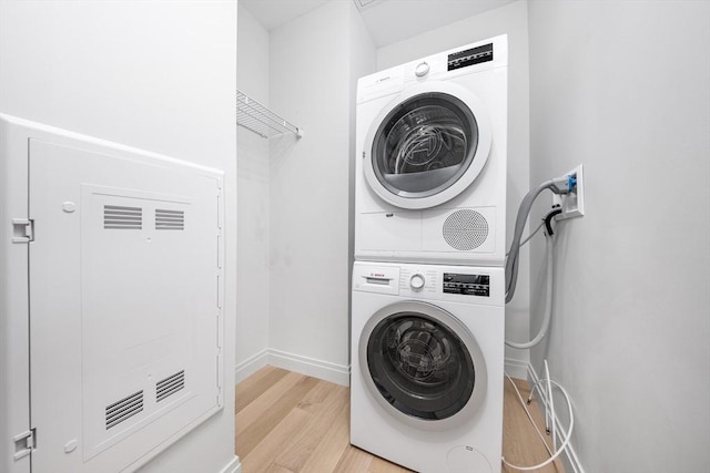 laundry room featuring baseboards, stacked washer and dryer, laundry area, and light wood finished floors