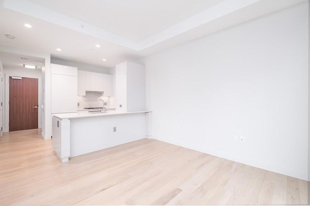 kitchen featuring a peninsula, white cabinets, light wood-style floors, and light countertops