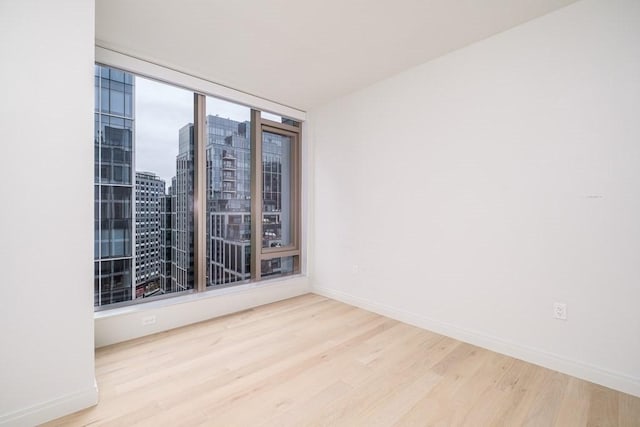 unfurnished room with baseboards, a city view, and wood finished floors