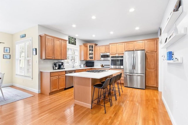 kitchen with stainless steel appliances, light countertops, a center island, a breakfast bar, and light wood-type flooring