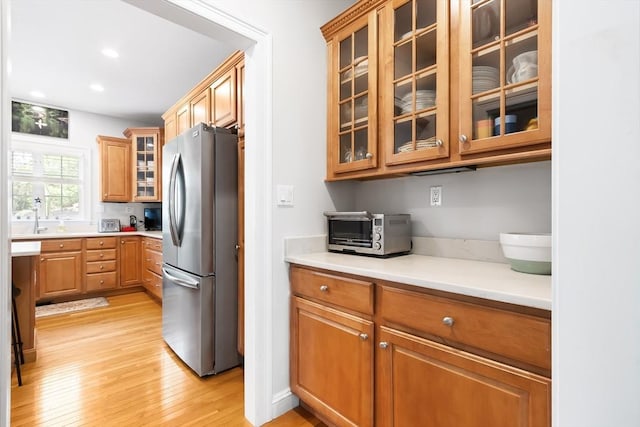 kitchen featuring freestanding refrigerator, light wood-type flooring, light countertops, glass insert cabinets, and recessed lighting