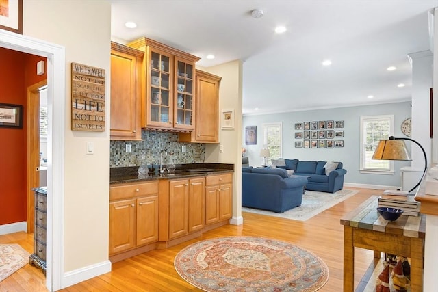 kitchen with light wood-style flooring, baseboards, tasteful backsplash, glass insert cabinets, and open floor plan