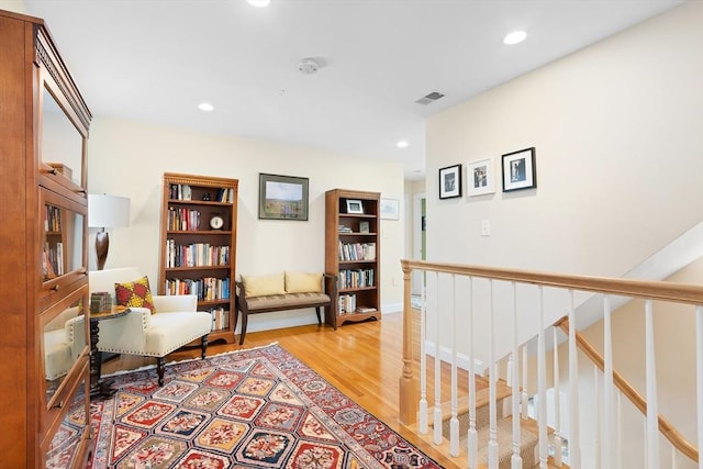 sitting room with light wood-type flooring, recessed lighting, and an upstairs landing