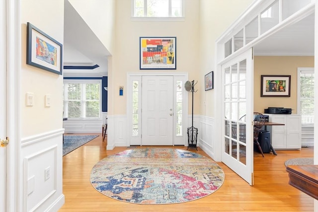 foyer with wood finished floors, a wainscoted wall, crown molding, and a decorative wall