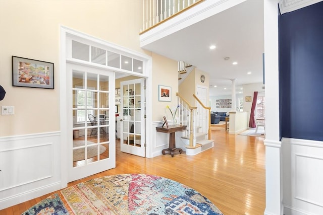doorway with wood finished floors, wainscoting, stairway, decorative columns, and a decorative wall